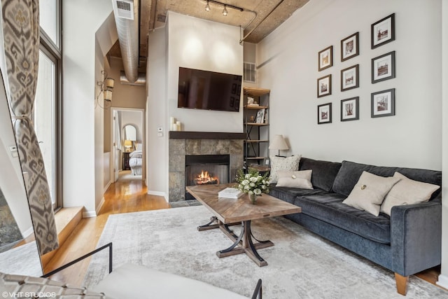 living room with a fireplace, light hardwood / wood-style floors, a towering ceiling, and rail lighting