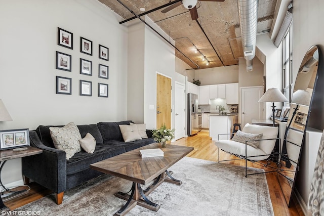 living room featuring a towering ceiling, light wood-type flooring, rail lighting, ceiling fan, and sink