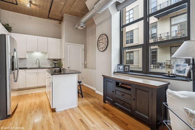 kitchen featuring white cabinetry, stainless steel fridge, a kitchen island, and a high ceiling