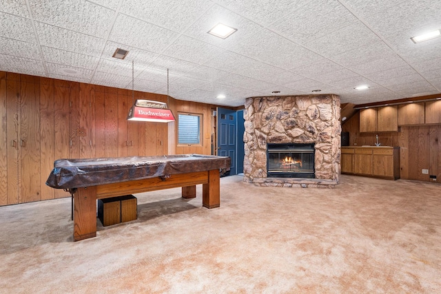 rec room featuring carpet floors, wood walls, and a stone fireplace