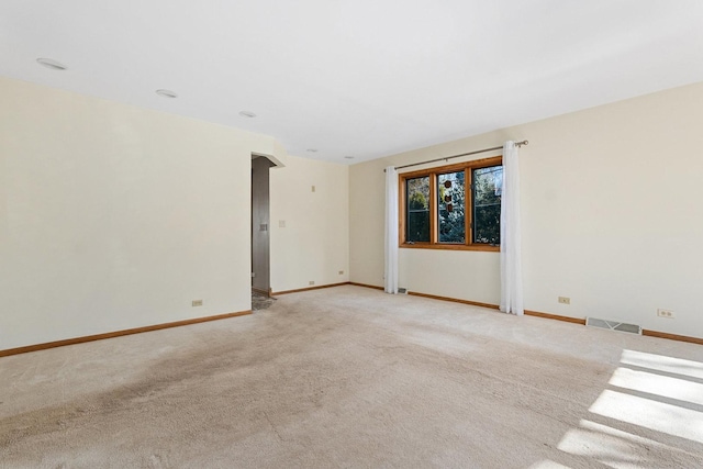 unfurnished room featuring arched walkways, light colored carpet, visible vents, and baseboards