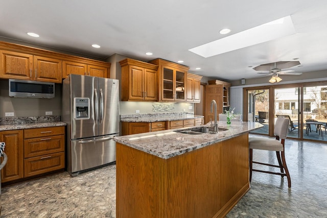 kitchen with a skylight, glass insert cabinets, appliances with stainless steel finishes, brown cabinets, and a sink