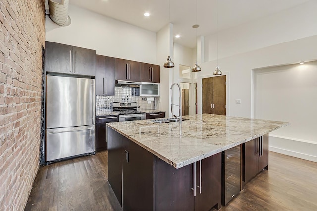 kitchen featuring stainless steel appliances, a kitchen island with sink, sink, decorative light fixtures, and a high ceiling