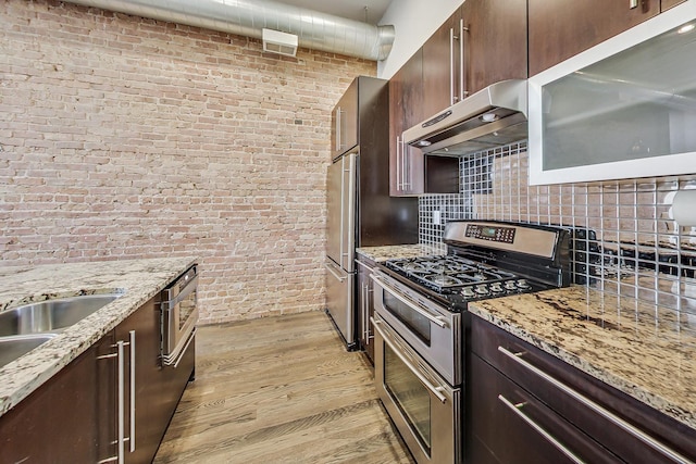 kitchen featuring light stone counters, light wood-type flooring, stainless steel appliances, and brick wall