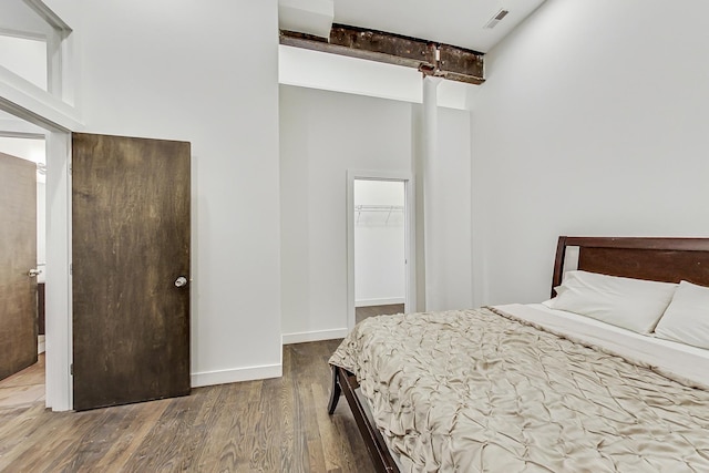 bedroom featuring beam ceiling, a walk in closet, a closet, and hardwood / wood-style floors