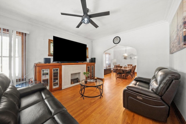 living room featuring hardwood / wood-style flooring, a brick fireplace, ceiling fan, and crown molding