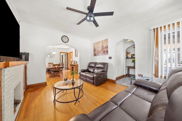 living room with a brick fireplace, light hardwood / wood-style floors, ceiling fan with notable chandelier, and ornamental molding