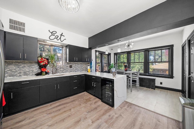 kitchen featuring decorative backsplash, light wood-type flooring, kitchen peninsula, and beverage cooler