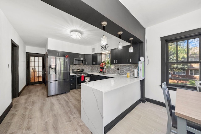 kitchen with kitchen peninsula, backsplash, light stone counters, stainless steel appliances, and pendant lighting