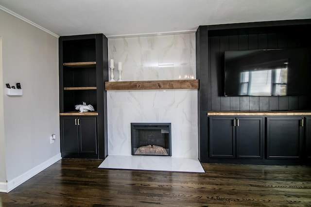 unfurnished living room featuring a fireplace, crown molding, built in features, and dark wood-type flooring