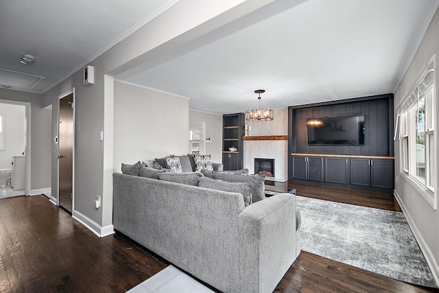 living room with a large fireplace, a chandelier, dark hardwood / wood-style floors, and ornamental molding