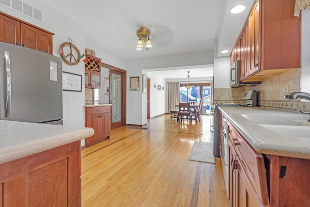 kitchen featuring ceiling fan, appliances with stainless steel finishes, tasteful backsplash, light wood-type flooring, and sink