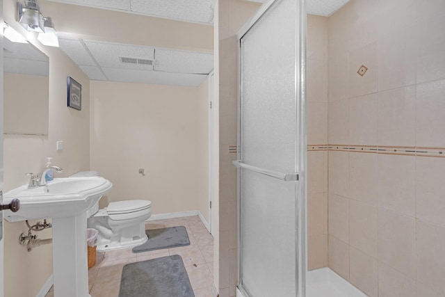 bathroom with a drop ceiling, tile patterned floors, a shower with door, and toilet