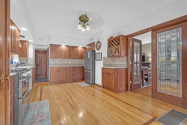 kitchen featuring ceiling fan, appliances with stainless steel finishes, light wood-type flooring, and tasteful backsplash