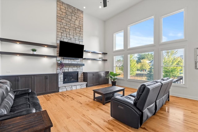 living room featuring ceiling fan, a towering ceiling, a fireplace, and light hardwood / wood-style flooring