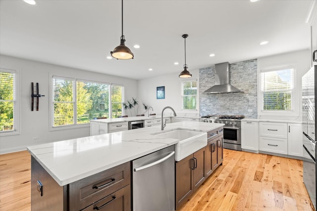 kitchen featuring a center island with sink, white cabinets, wall chimney range hood, and stainless steel appliances