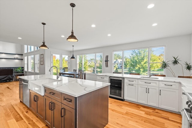 kitchen with beverage cooler, a kitchen island with sink, sink, white cabinetry, and hanging light fixtures