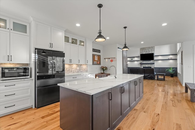 kitchen with tasteful backsplash, black fridge, light stone counters, a center island with sink, and white cabinetry