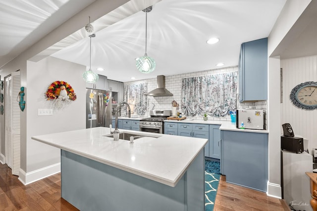 kitchen featuring sink, wall chimney exhaust hood, decorative backsplash, appliances with stainless steel finishes, and decorative light fixtures