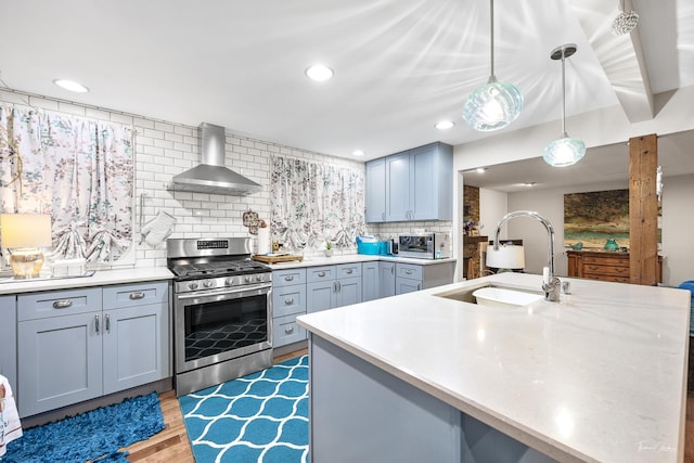 kitchen featuring backsplash, gas stove, sink, wall chimney range hood, and pendant lighting