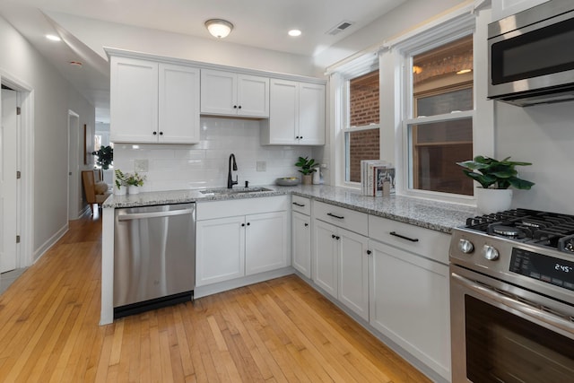 kitchen with light stone countertops, light wood-type flooring, stainless steel appliances, sink, and white cabinets