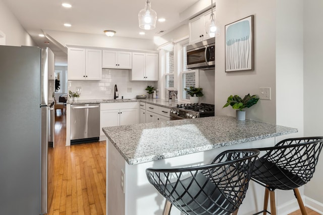 kitchen featuring white cabinets, pendant lighting, kitchen peninsula, and stainless steel appliances