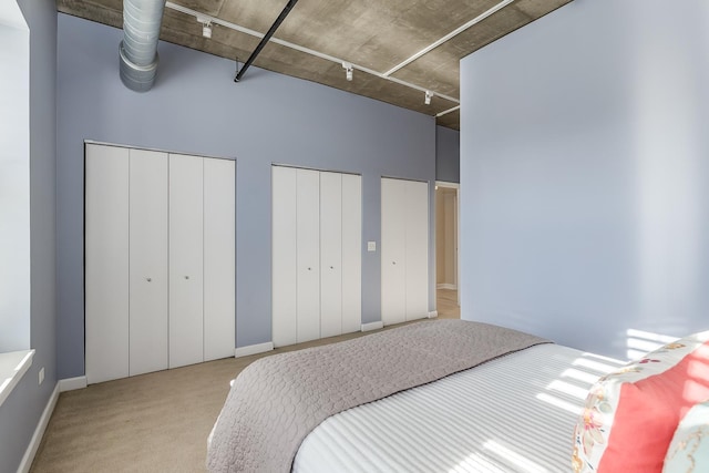 bedroom featuring a high ceiling, light carpet, and multiple closets