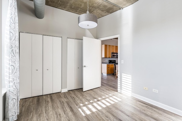 unfurnished bedroom with multiple closets, light hardwood / wood-style flooring, and a towering ceiling