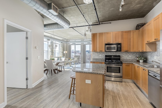 kitchen with light stone counters, light hardwood / wood-style flooring, a center island, stainless steel appliances, and sink