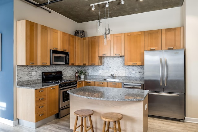 kitchen featuring dark stone countertops, stainless steel appliances, a center island, a breakfast bar, and sink