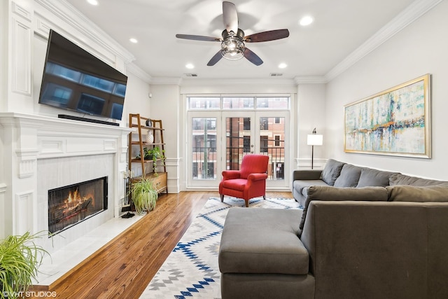 living room with a tiled fireplace, ceiling fan, light hardwood / wood-style floors, and ornamental molding