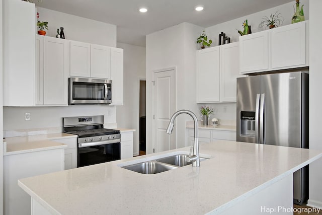 kitchen featuring a center island with sink, sink, light stone counters, white cabinetry, and stainless steel appliances