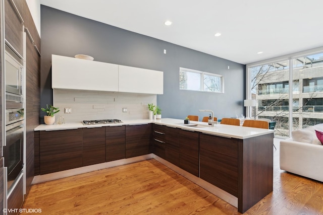 kitchen with sink, tasteful backsplash, light hardwood / wood-style flooring, kitchen peninsula, and white cabinets