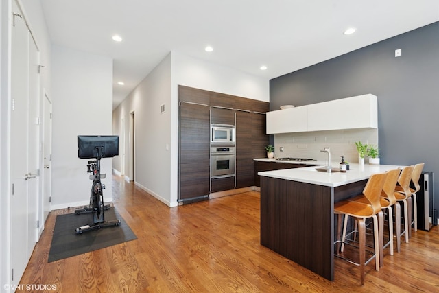 kitchen with a breakfast bar, white cabinets, light hardwood / wood-style flooring, dark brown cabinetry, and stainless steel appliances