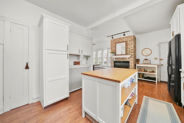 kitchen with rail lighting, white cabinetry, black fridge, wooden counters, and a brick fireplace