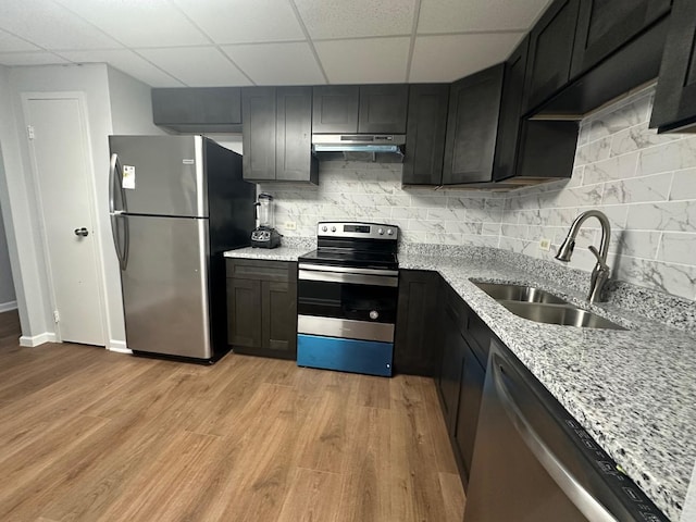 kitchen with a drop ceiling, sink, decorative backsplash, light stone countertops, and appliances with stainless steel finishes