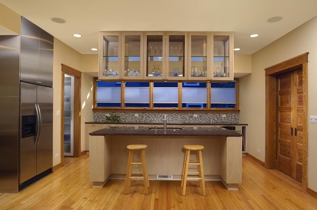 kitchen featuring a breakfast bar, a kitchen island with sink, built in fridge, light wood-type flooring, and tasteful backsplash