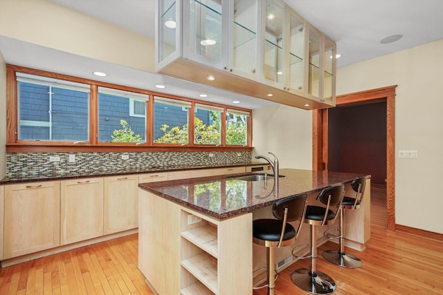 kitchen with light brown cabinets, backsplash, an island with sink, and sink