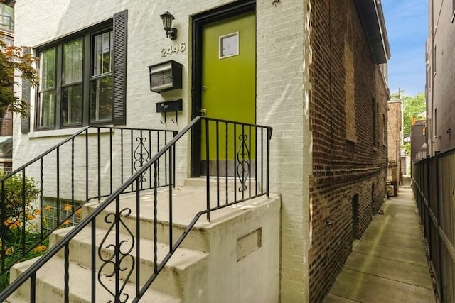 view of exterior entry featuring brick siding and fence