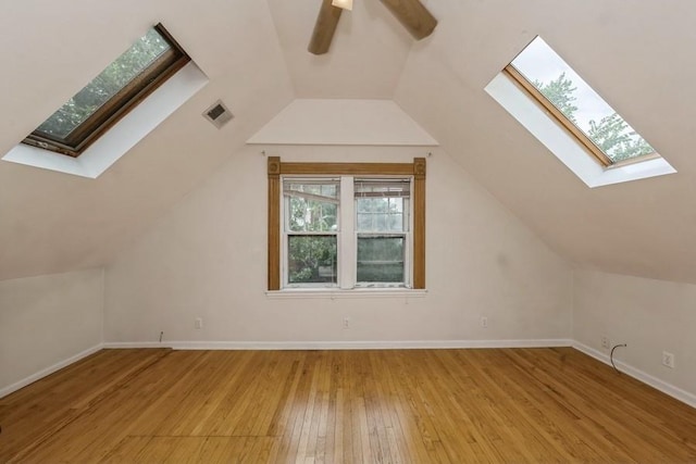 additional living space with vaulted ceiling with skylight, ceiling fan, and light hardwood / wood-style flooring