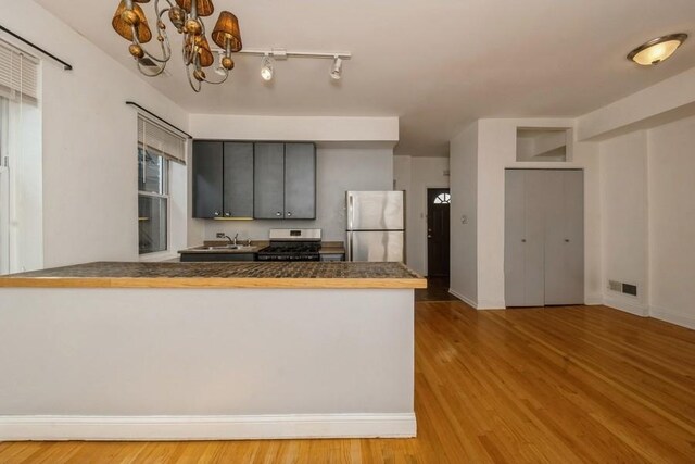 kitchen featuring sink, appliances with stainless steel finishes, a notable chandelier, light hardwood / wood-style floors, and kitchen peninsula