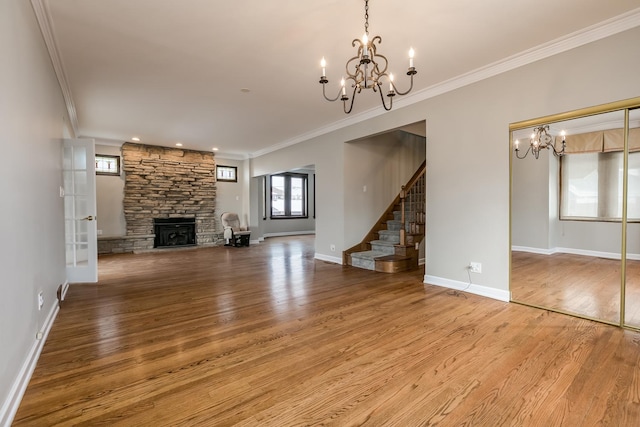 unfurnished living room with wood-type flooring, a stone fireplace, ornamental molding, and a notable chandelier