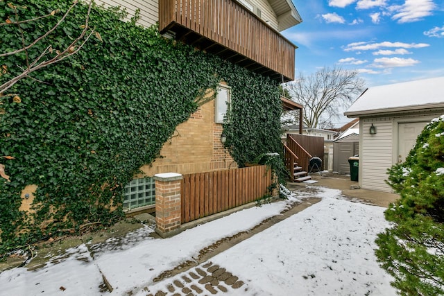 view of snow covered exterior with a balcony and a storage shed