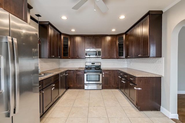 kitchen featuring appliances with stainless steel finishes, light stone counters, dark brown cabinetry, ceiling fan, and light tile patterned floors