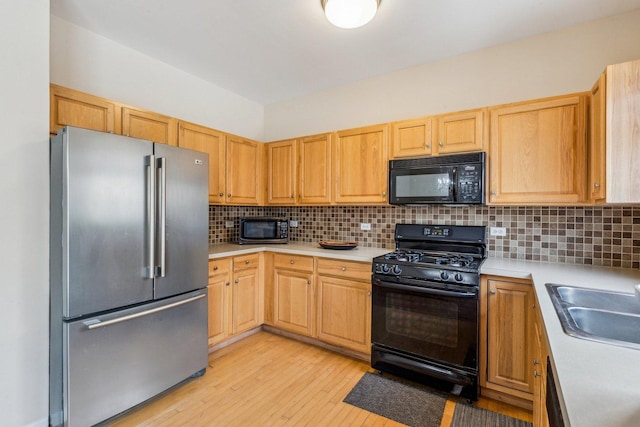 kitchen with light brown cabinetry, light wood-type flooring, tasteful backsplash, sink, and black appliances