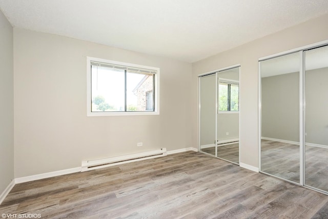 unfurnished bedroom with multiple closets, hardwood / wood-style floors, a baseboard radiator, and multiple windows