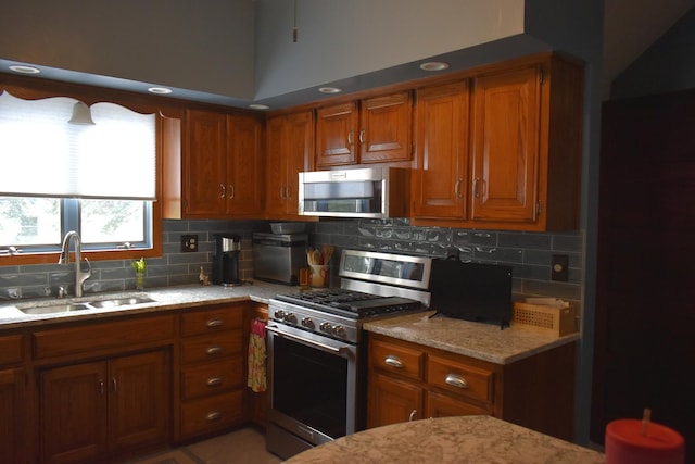 kitchen with decorative backsplash, light stone counters, sink, and appliances with stainless steel finishes