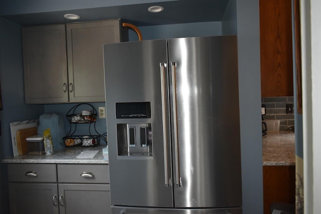 kitchen with decorative backsplash, gray cabinets, light stone counters, and stainless steel fridge with ice dispenser