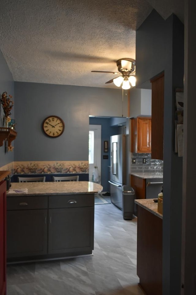 kitchen with backsplash, stainless steel refrigerator, ceiling fan, and a textured ceiling