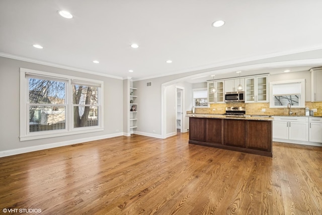 kitchen featuring stainless steel appliances, light stone counters, light hardwood / wood-style flooring, a kitchen island, and ornamental molding